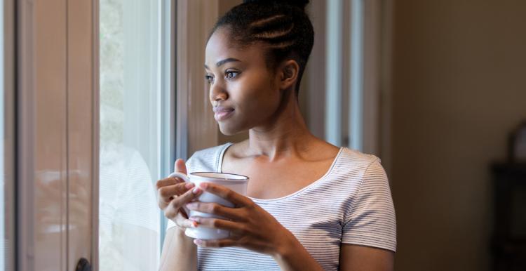 woman standing in front of a window holding a cup of tea