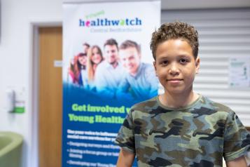 Young boy stood in front of a Healthwatch banner Young boy stood in front of a Healthwatch banner Young boy stood in front of a Healthwatch banner